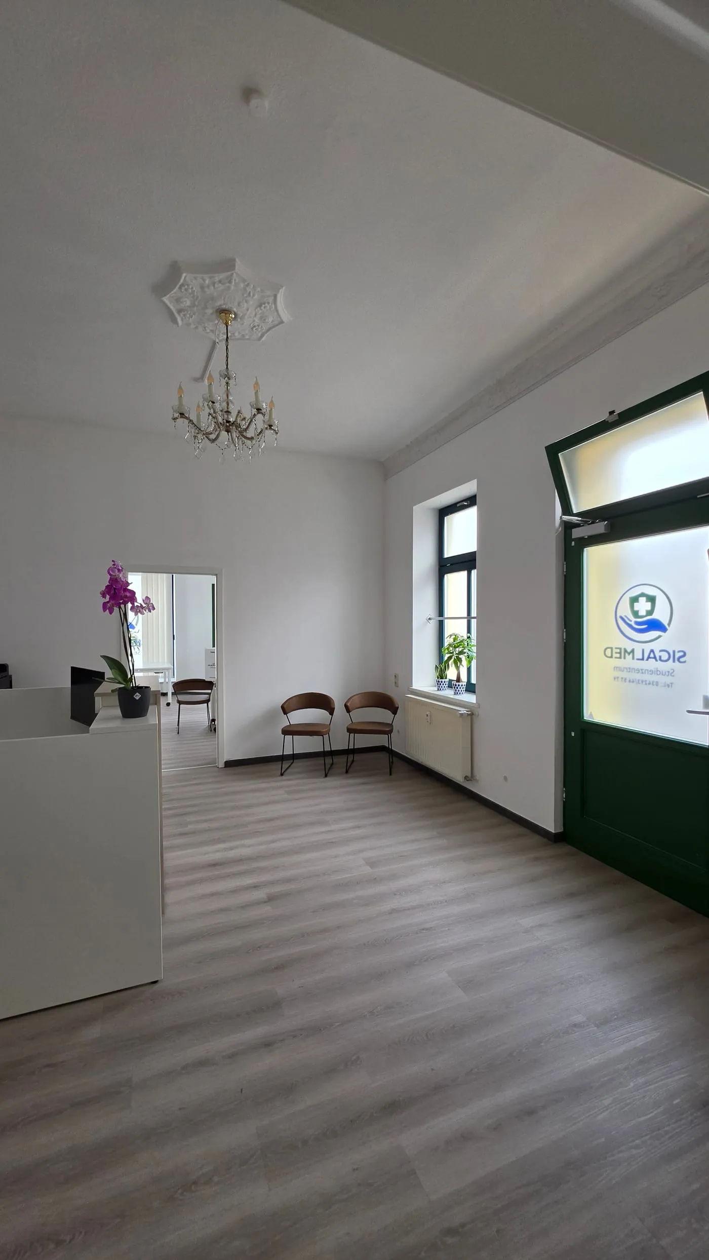 Empfang und Wartebereich des Studienzentrums Naunhof mit Tresen, zwei Stühlen und der Eingangstür mit SIGALMED-Logo