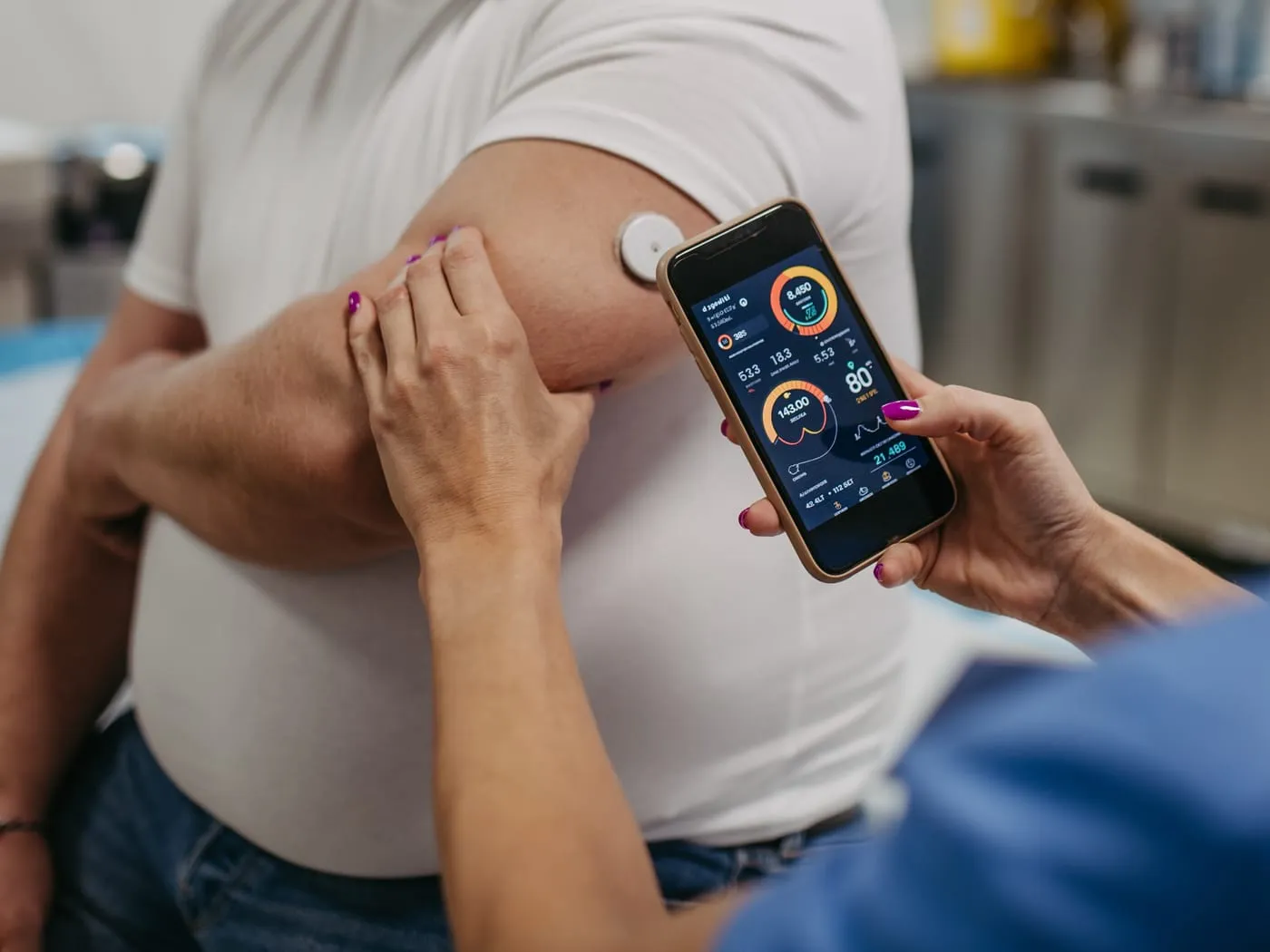 Pflegekraft liest einen Glukosesensor am Oberarm mit dem Smartphone aus