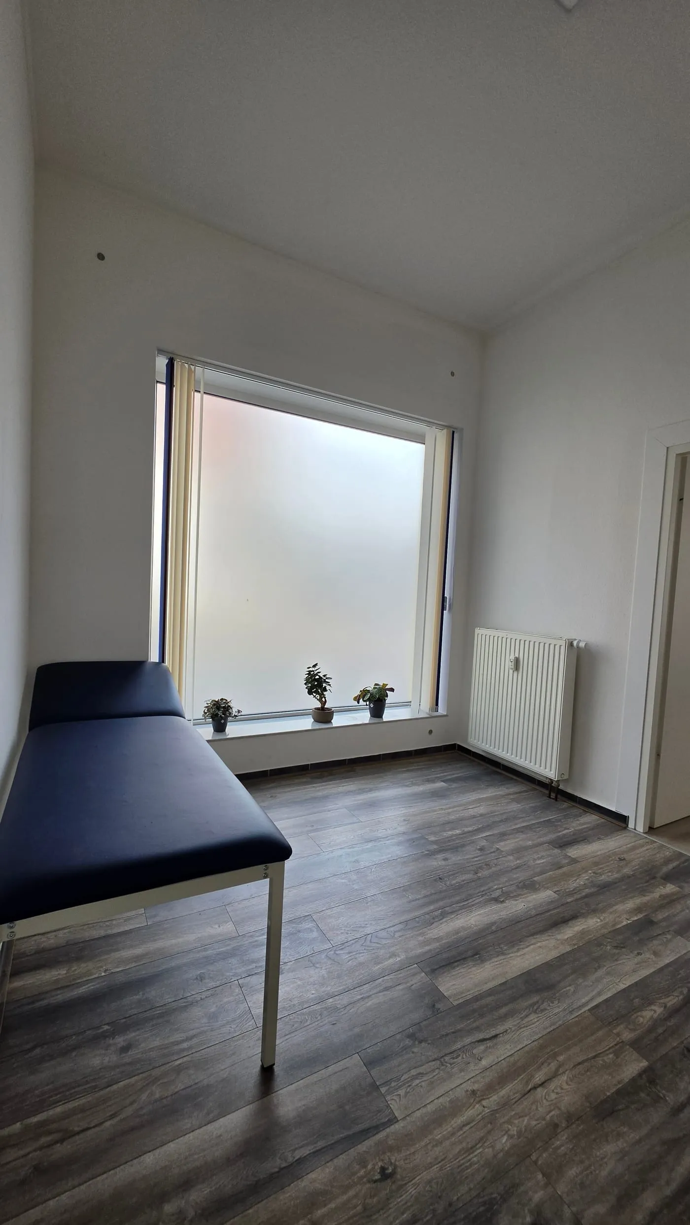 Heller Untersuchungsraum mit Liege und großem Fenster